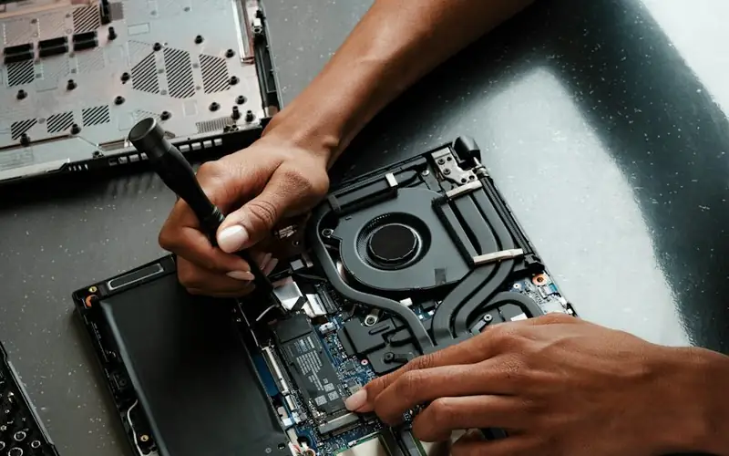 Hands fitting a part inside an opened laptop